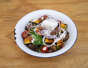 Healthy food. Top view of a gourmet salad with sliced cabbage, roasted eggplant, red onion, almonds, arugula, pumpkin and a poached egg in a white bowl on the wooden table.