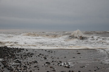 Large waves crashing onto the beach during a storm with a dramatic sky background. Taken in Cleveleys Lancashire England. 