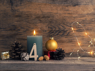 Candle of the fourth Advent burns, pine cones and Christmas decoration on wood