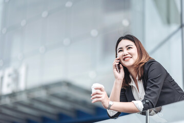 Young Asian businesswoman talking on phone and using tablet. Beautiful woman passenger has mobile call and discusses something with smile, holds coffee in hand