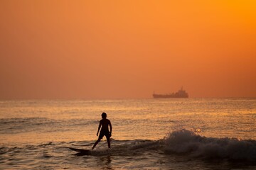 Person surfing in the ocean at sunset