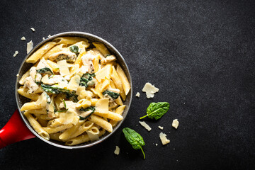 Pasta penne with chicken and spinach in creamy sauceon black table. Top view with copy space.