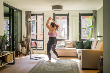 Fototapeta na wymiar Body positive woman doing jumping jacks or star jump exercise at home