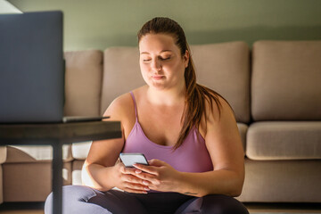 Calm fat woman sitting at the living room and looking at her smartphone