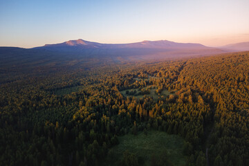 Aerial view of mountain range and forest beautifully lightened by the rising sun under clear morning sky
