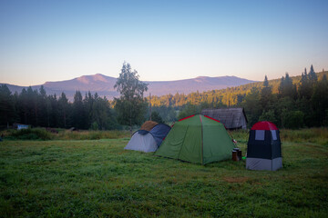 Tourist camp with tents in a clearing in a forest with a mountain range lightened by the rising sun in the background