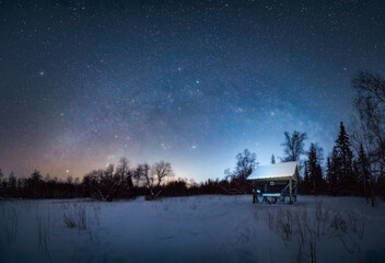 Mlky way Arc in the night sky above snow-covered garden house in winter forest