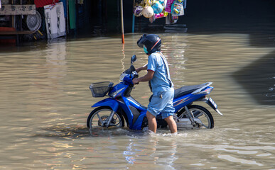 A man pushes a motorcycle along a flooded street