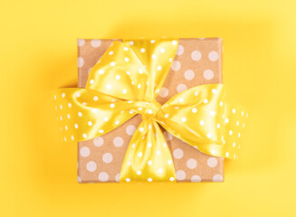 One holiday wrapped polka dot kraft gift box with yellow polka dot bow on yellow. Top view.