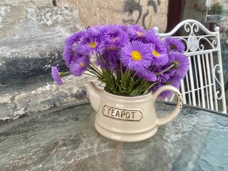 Purple asters bouquet in a decorative vase teapot on a table.