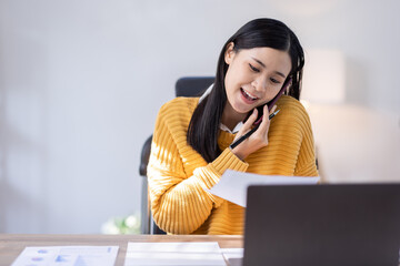 Young business Asian woman working in home office, making phone call to potential client, having...