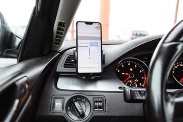 Smartphone with navigation route on screen mounted on phone holder at car dashboard.