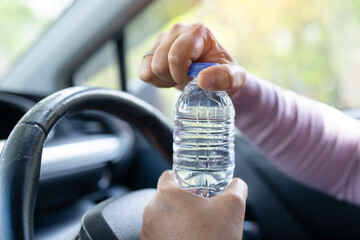 Asian woman driver holding bottle for drink water while driving a car. Plastic hot water bottle...