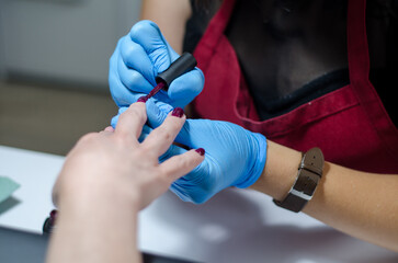 Female manicurist in blue gloves works with young hands and nails under a bright lamp. Process of applying gel polish on nails