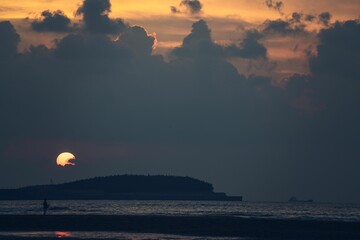 Horizontal image of sea and island at sunset with dark clouds.