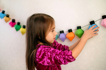 The girl hangs a hand-made garland of paper on the wall. Cardboard crafts and Christmas...