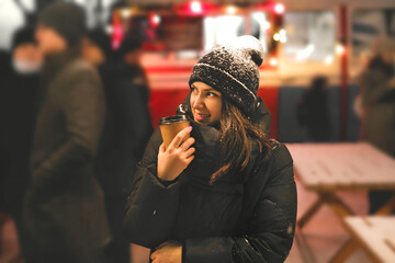 A woman in the crowd on the street looks away holding a glass of hot tea. A girl's hat in the snow....