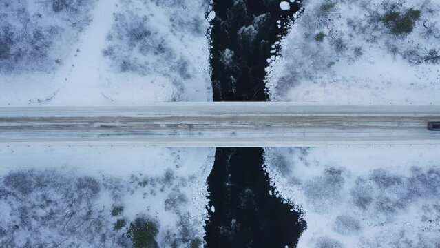 an arctic river rapid with icy dark water in northern finland utsjoki with snowy rocks by the side of the water filmed with a drone in 4k in lapland mavic pro 2 car passing by over the bridge