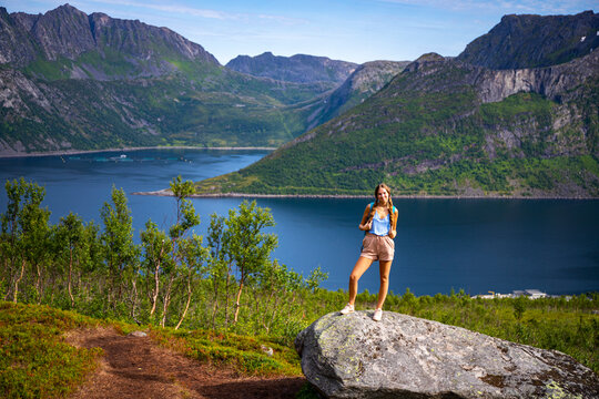 backpacker girl hiking hesten trailhead overlooking the town of fjordgard and mighty mountains in norway, senja island hiking, famous segla mountain