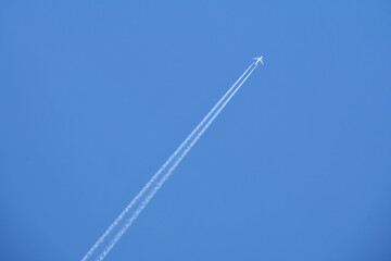 A large jet airplane flying through a clear blue sky with vapor trails 