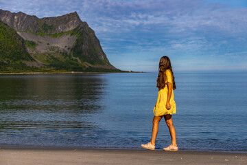 a beautiful girl in a yellow dress walks on a beach surrounded by mighty mountains on the island of senja in norway, holiday in the norwegian fjords, steinfjord