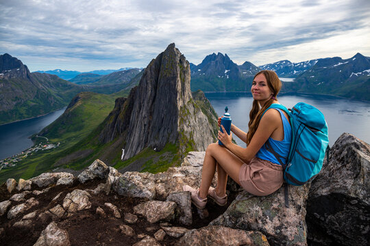 a beautiful girl sits on the rocks enjoying the view of the famous segla mountain in norway, senja island; hesten trail head, the famous norwegian fjords with mighty mountains above the sea