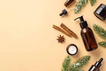 Winter skincare cosmetics concept. Top view photo of amber bottles without label cream jars fir branches in hoarfrost cinnamon sticks and anise on isolated beige background with empty space