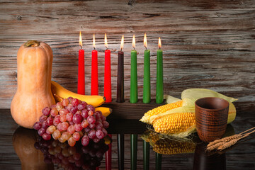 Kwanzaa holiday concept with traditional lit candles, pumpkin, corns, grapes, banana, bowl and of wheat with reflection on black background