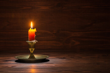 burning old candle with vintage brass candlestick on wooden background in minimalist room interior,...