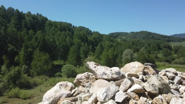 Stedicam pan shot of climbing the one of small rocky mountains with mountain forests and hills around when sunny summer and clear sky