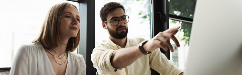 Businessman pointing at blurred computer near young intern in office, banner.