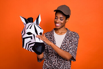 Portrait of attractive trendy cheery girl holding in hands 3d zebra mask isolated over bright orange color background