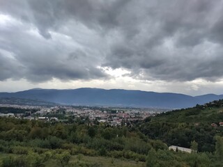 Cityscape view of East Sarajevo and green landscape with mountains and dark cloudy sky