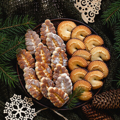 Christmas shortbread cookies with fir tree branches, cones, wooden tree toys on a dark knitted background.