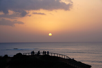 people on a hill watching the sunset over the ocean                             