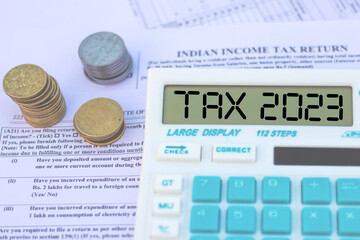 Tax 2023 text on calculator screen, with stack of coins and ITR Indian Income Tax form 2023.