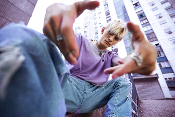 A teenage boy is sitting and posing in urban exterior surrounded by the buildings.