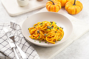 A light grey deep bowl with vegan pasta spaghetti carbonara with orange pumpkin sauce and fresh green herbs on marble board on pastel background