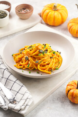 A light grey deep bowl with vegan pasta spaghetti carbonara with orange pumpkin sauce and fresh...