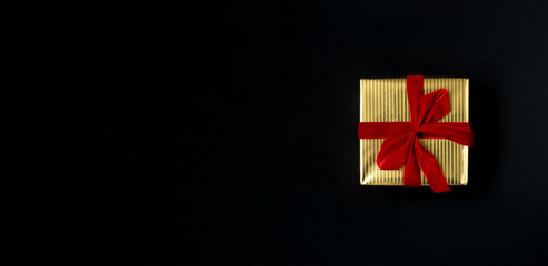 Golden gift box with red ribbon on a black background top view