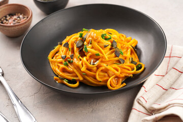 A deep black bowl with vegan pasta spaghetti carbonara with orange pumpkin sauce and fresh green...