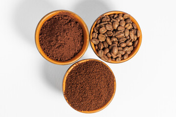 Cups with roasted coffee beans and ground coffee, white background and copy space.