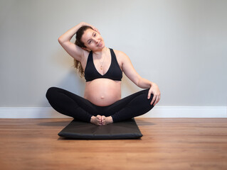 Pregnant woman stretching her trapezius muscles - obrazy, fototapety, plakaty