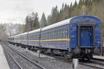 Tourist passenger train at the station waiting for passengers, with a steam locomotive smoking in the distance