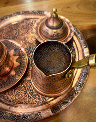 Hot coffee in traditional turkish copper coffee cezva, authentic arabic  coffee utensil set, coffee pot on wooden table