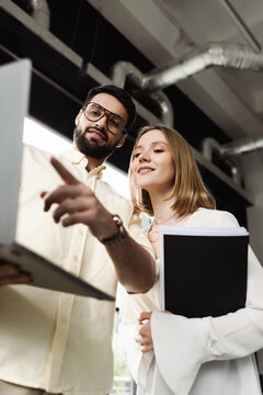 Low angle view of businessman pointing at laptop near new worker with paper folder in office.