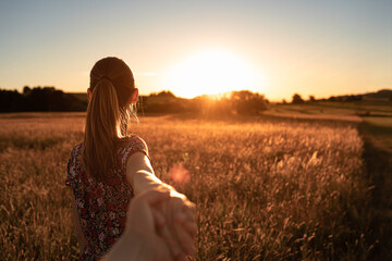 Come follow me. Couple holding hands walking in a field into the sunset. 