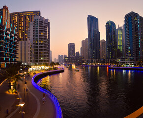 Obraz premium Dubai, UAE - 12th october, 2022: Dubai Marina skyline with illuminated sky scrappers,buildings and moving boats showing reflection on water captured from Marina Mall , Dubai, UAE.