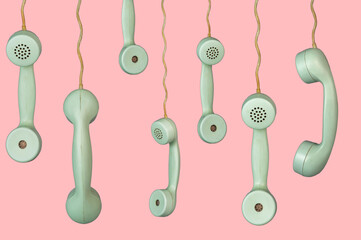 Many old telephone handsets from rotary landlines hanging from cords on pink background. Plastic...