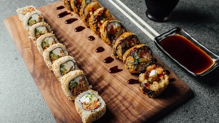 Gordijnen Closeup of a set of delicious fresh sushi rolls, chopsticks, and soy sauce on a  wooden board © Aleksandrs Muiznieks/Wirestock Creators